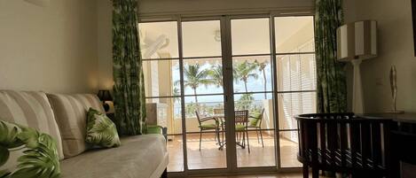 A living room with a sofa, a dining table, and a view of a balcony with chairs and a table.