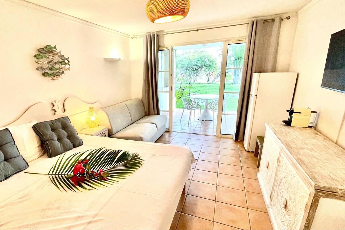 Ein Schlafzimmer mit Bett, einer Couch, einem Schminktisch und einer Glastür, die auf eine Terrasse mit Gartenmöbeln führt.