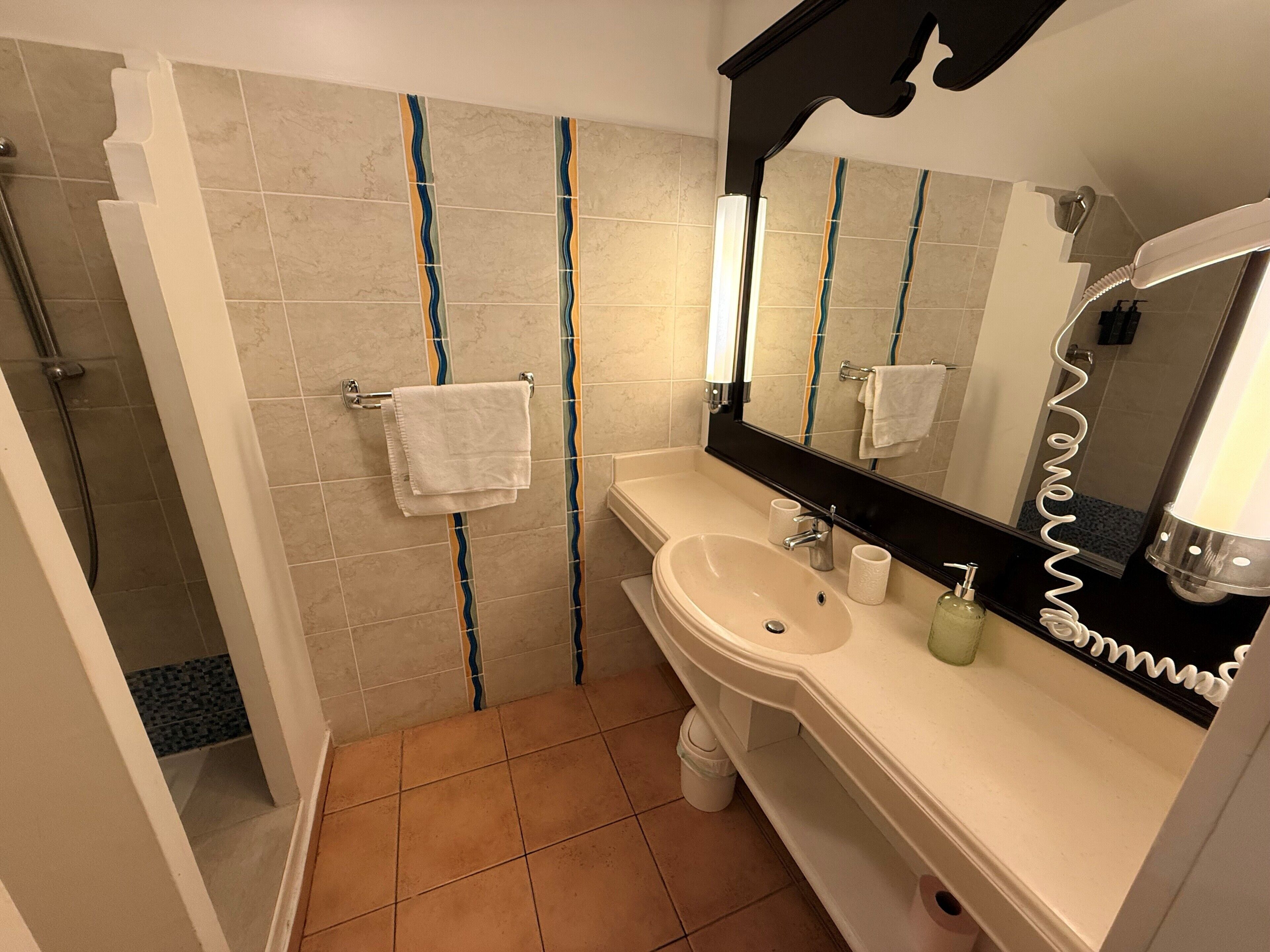 A bathroom with a sink, mirror, towel rack, and shower.