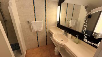 A bathroom with a sink, mirror, towel rack, and shower.