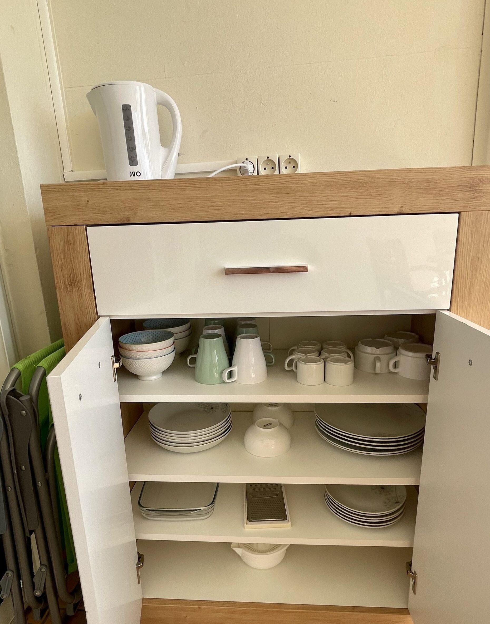Un armario de cocina con interior blanco, una encimera de madera y una tetera blanca encima.