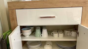 Un armario de cocina con interior blanco, una encimera de madera y una tetera blanca encima.