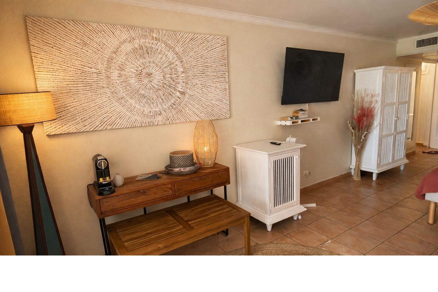 Un salon avec un banc en bois, une armoire blanche, un téléviseur fixé au mur et un élément décoratif mural.