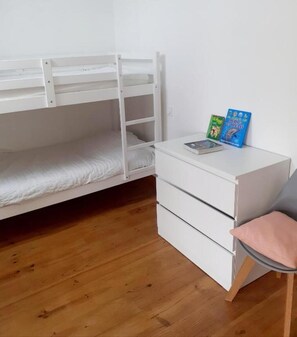 Una cama litera con colchón blanco, un escritorio blanco con cajones y dos libros sobre el escritorio.