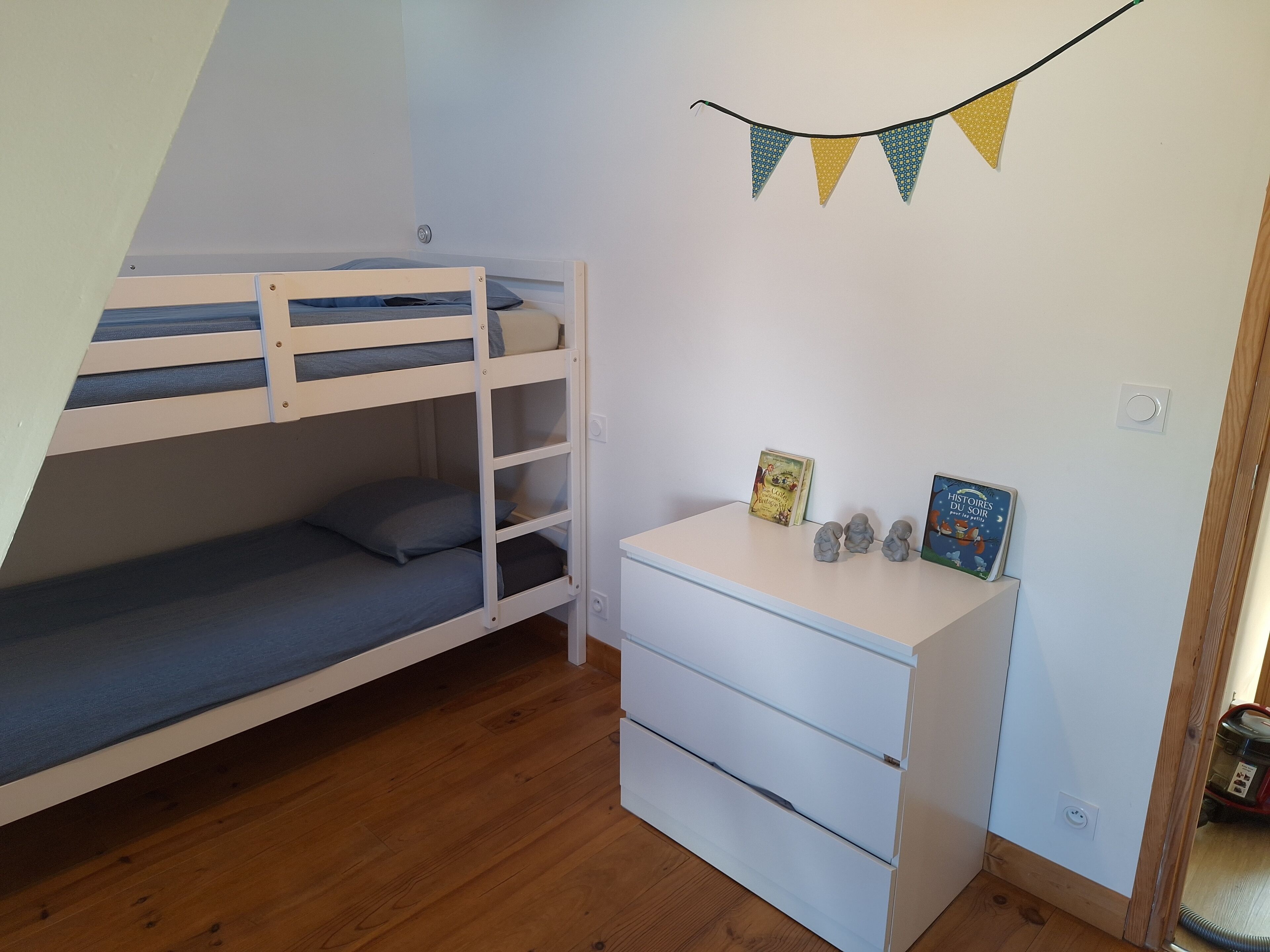 En våningssäng med ett skrivbord och lådor, en liten hylla med böcker och en rad triangulära flaggor som hänger på väggen.