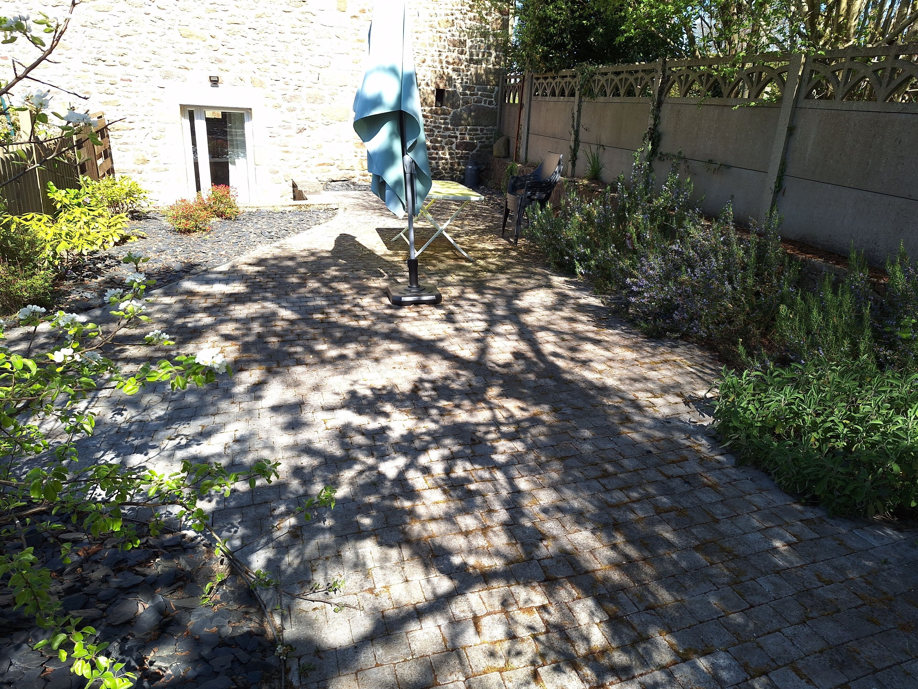 Ein gepflasterter Innenhof mit einer Steinmauer, einer überdachten Sitzgelegenheit und verschiedenen Pflanzen.