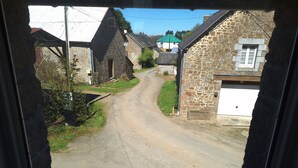 Eine schmale Landstraße, gesäumt von Steinhäusern mit traditioneller Architektur, strahlend blauer Himmel und ein deutlich sichtbares, grünes Dach.