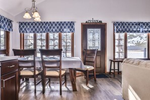 A dining area with a wooden table and chairs, a chandelier, and patterned window valances.