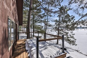 A wooden deck with a metal railing overlooking a snowy landscape and a body of water.