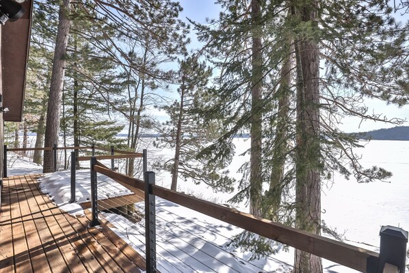 A wooden deck with a metal railing overlooking a snowy landscape and dense forest.