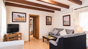 A living room with a TV, sofa, and coffee table. There are framed pictures on the walls and a door leading to another room. - Villa with pool very close to Es Trenc Beach (Campos)