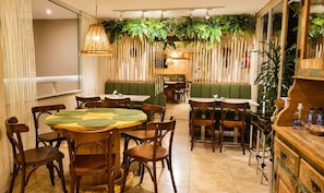 Un restaurant avec des tables rondes, des banquettes vertes et des plantes suspendues.