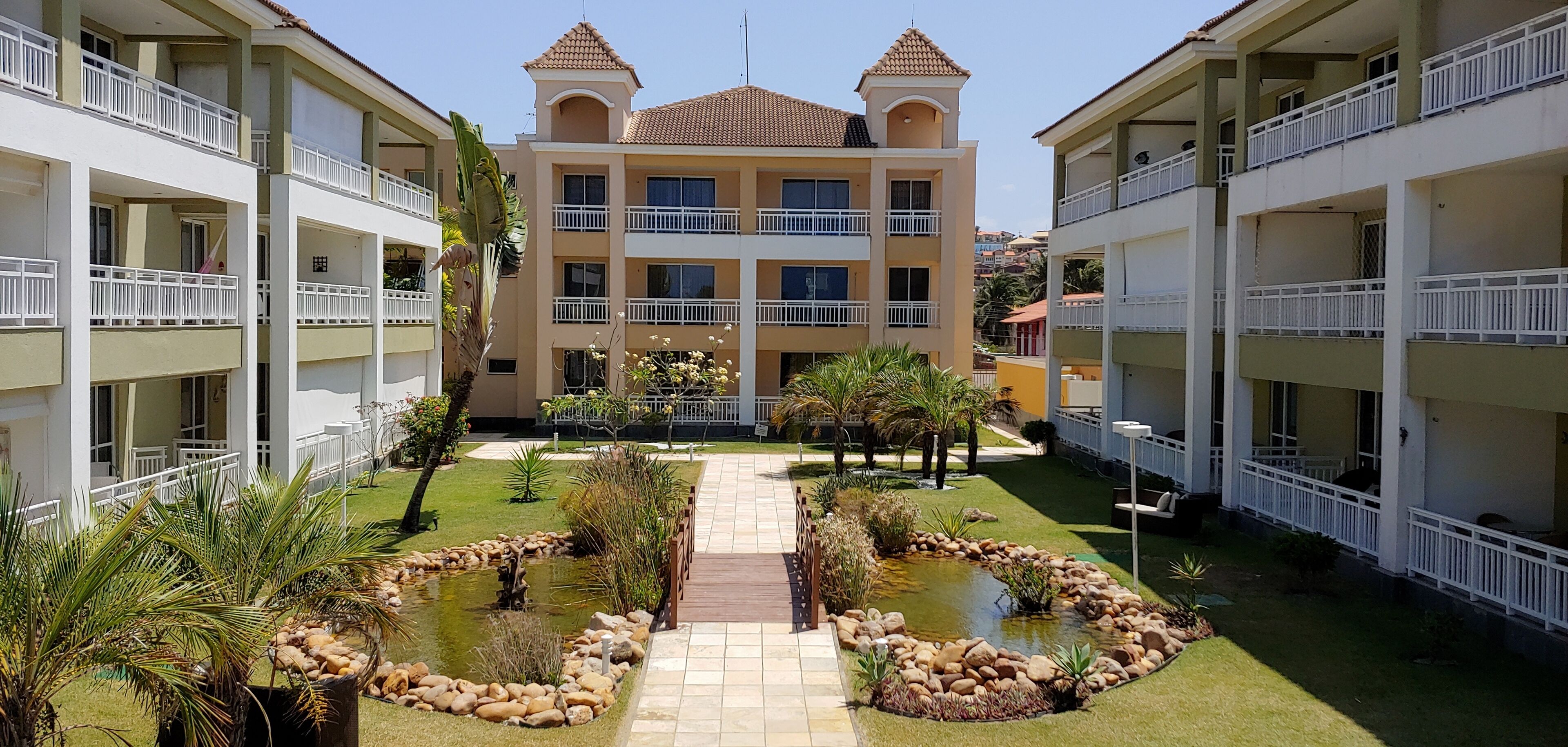 A hotel with a central courtyard featuring a small pond, surrounded by greenery and palm trees.