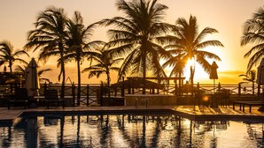 A pool area with palm trees and a sunset in the background. - Atlantic Palace Family inn (Aquiraz)