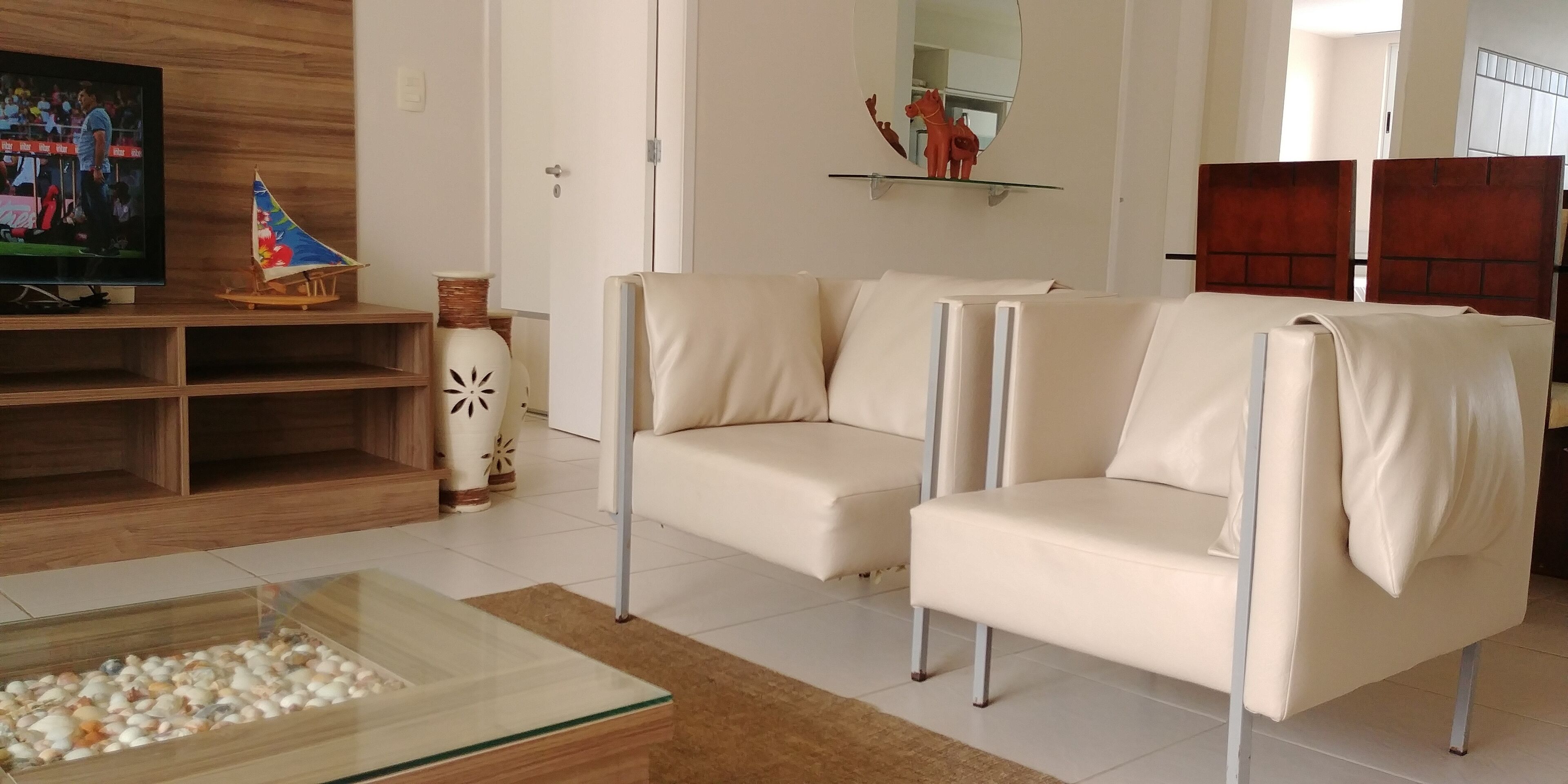 Een moderne woonkamer met een beige bank, een glazen salontafel en decoratieve objecten, waaronder een model zeilboot en vazen.