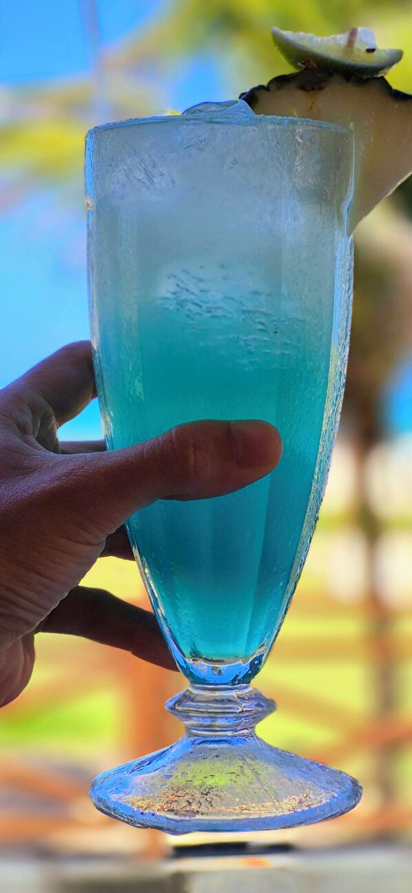 Eine Hand hält ein Glas mit blauer Flüssigkeit, möglicherweise ein Getränk, mit einem Limettenschnitz am Rand.