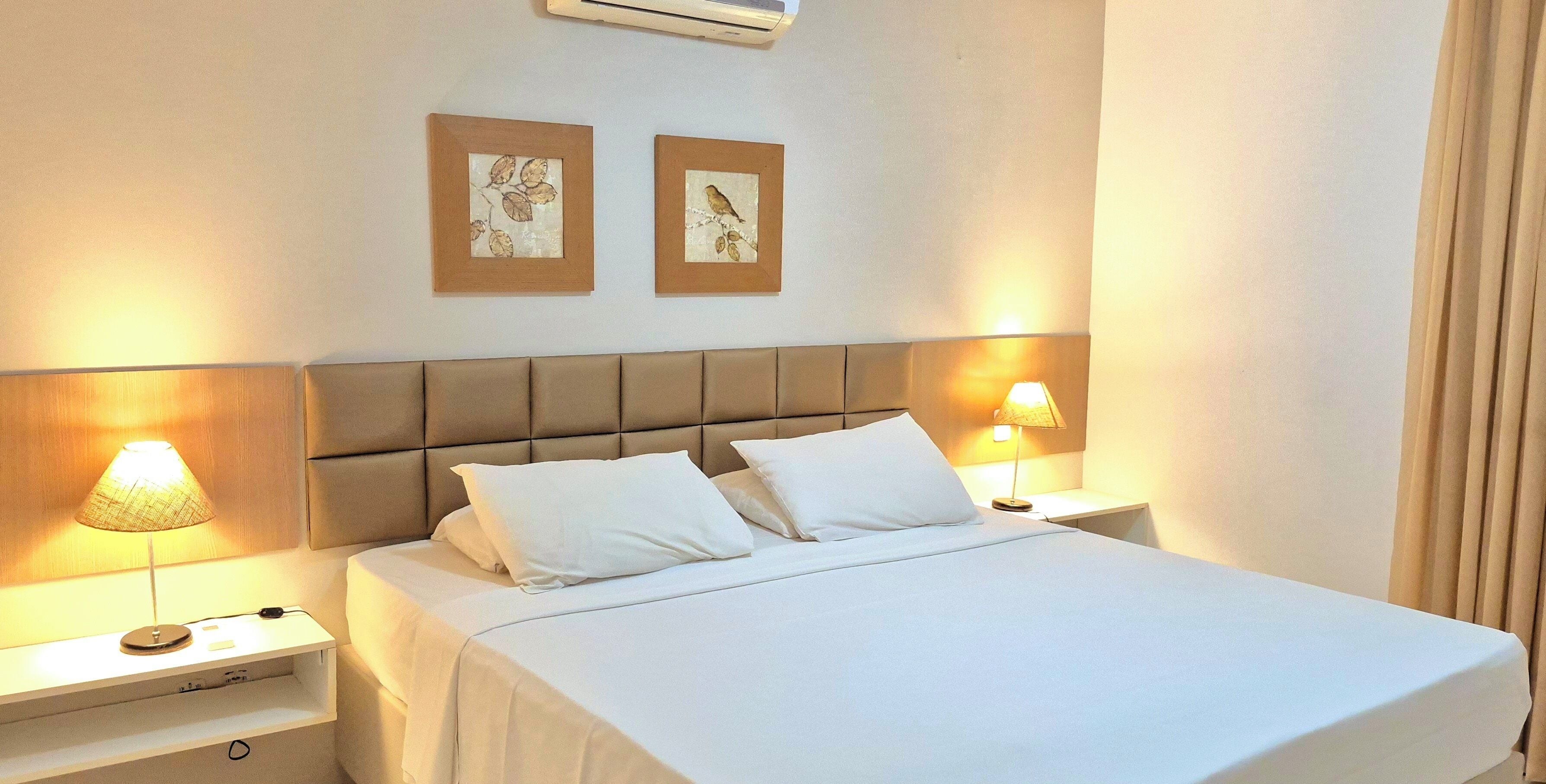 Una habitación de hotel con una cama, dos lámparas de noche, una mesita de noche y dos cuadros en la pared.