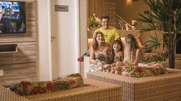 A family in a living room with a television, wicker furniture, and a staircase in the background.