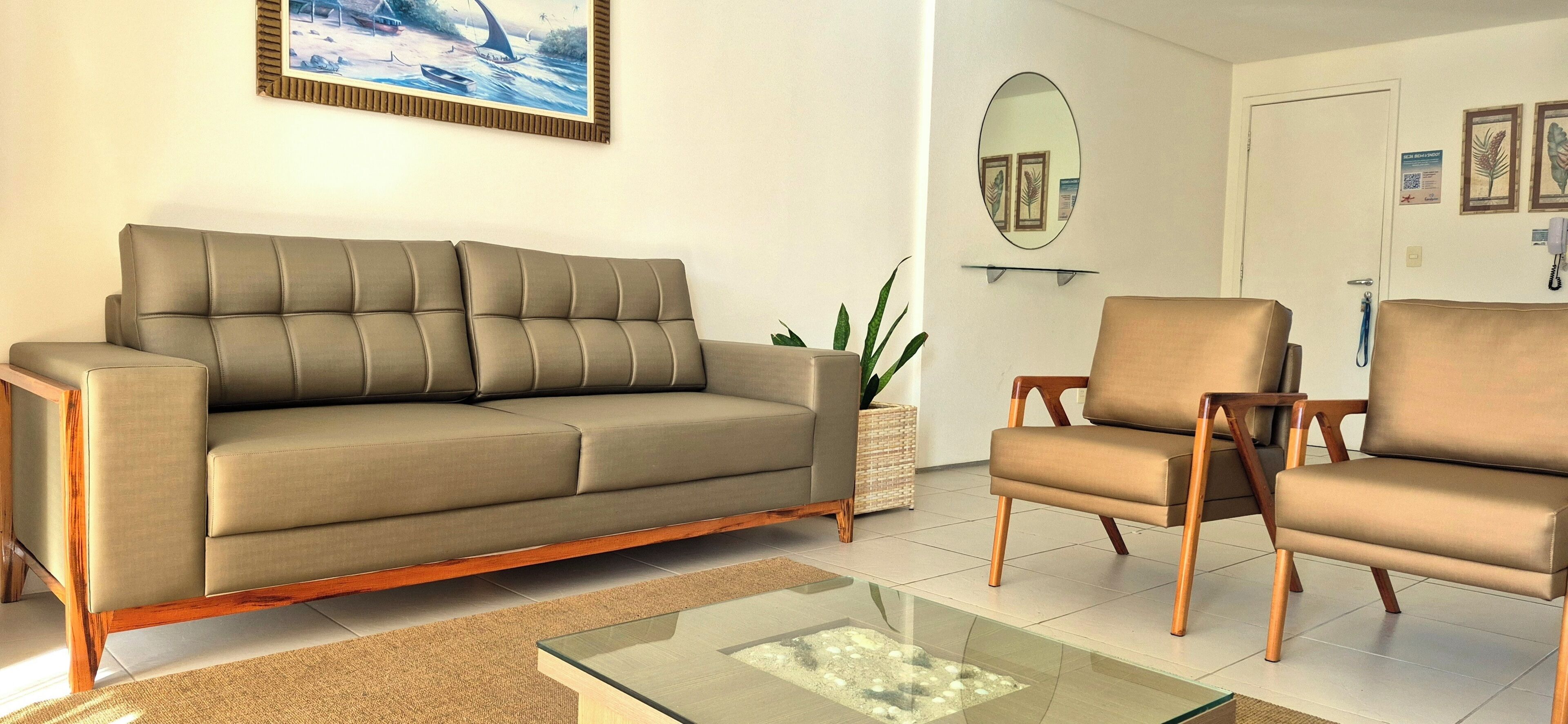 A living room with a sofa, two armchairs, a glass coffee table, a potted plant, and a painting on the wall.