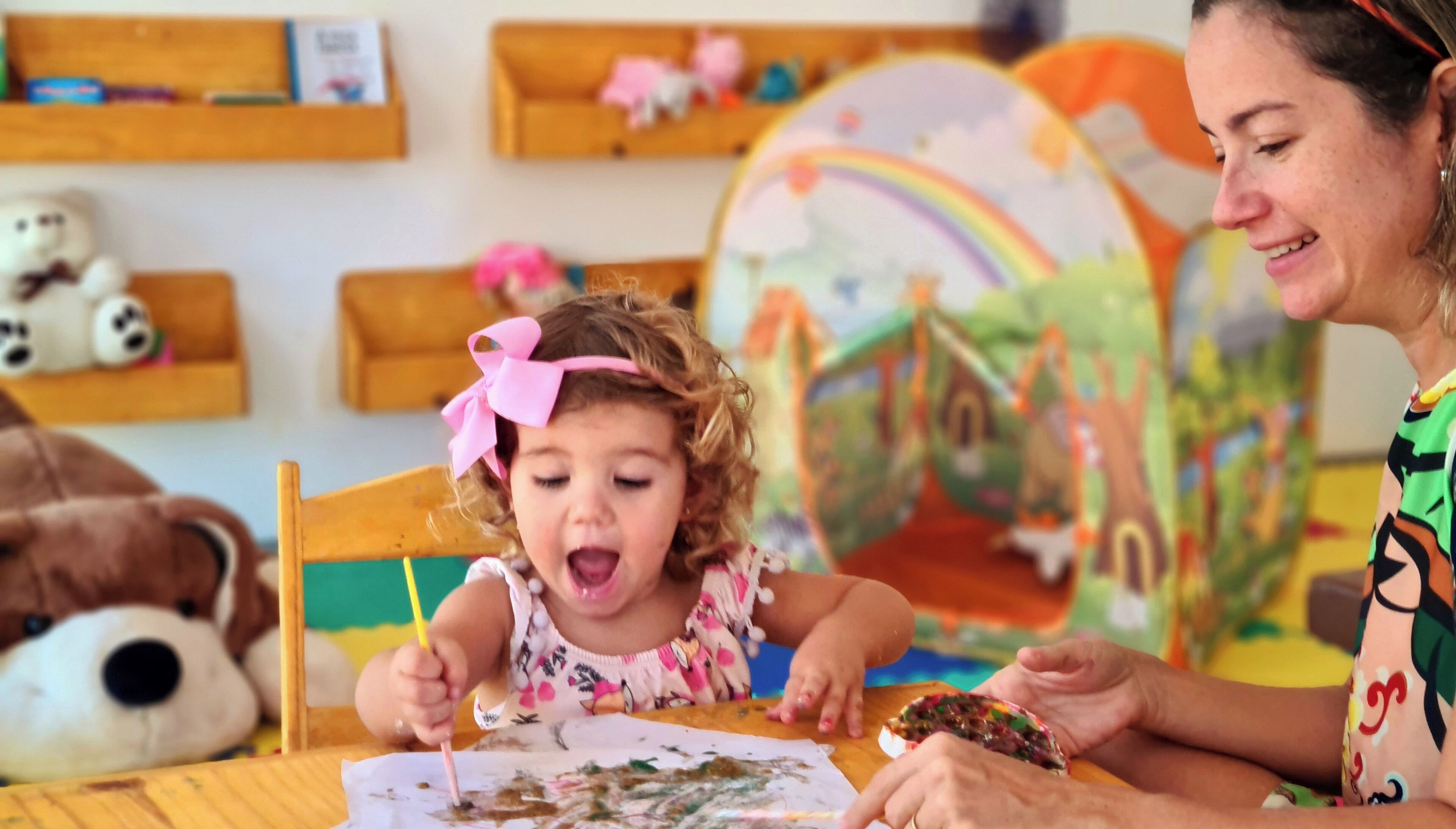 A child drawing at a table with a colorful mural in the background.