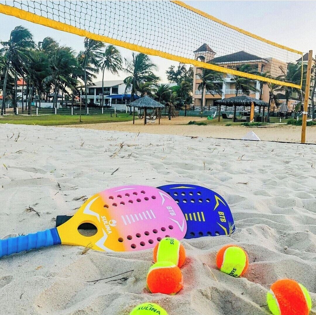 A beach volleyball net with two paddles and several volleyballs on the sand.