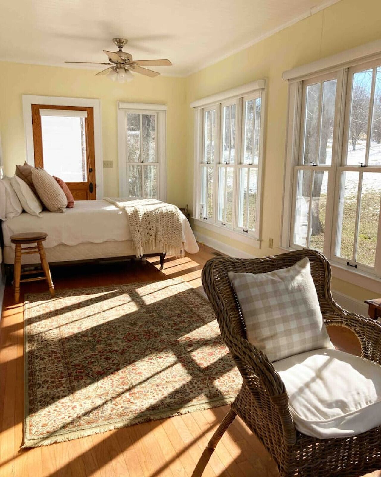 A bedroom with a bed, a chair, and large windows.