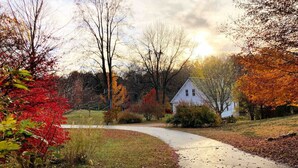 A rural road leading to a white house surrounded by autumn foliage.