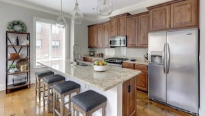 A kitchen with wooden cabinets, stainless steel appliances, a granite countertop, and pendant lighting. - Luxury Bay Street Condo featuring Dual King Suites (Savannah)