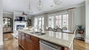 A spacious kitchen with a large island, wooden cabinets, and a dining area with chairs. - Luxury Bay Street Condo featuring Dual King Suites (Savannah)