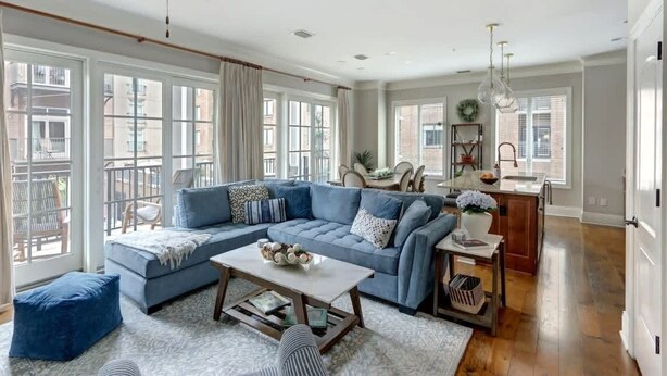 A spacious living room with a blue sectional sofa, a coffee table, and a view of the city through large windows. - Luxury Bay Street Condo featuring Dual King Suites (Savannah)