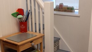 A wooden shelf unit with kitchen utensils, a red container, and a small table with a black surface. - Cosy Mews House Close to Harbour (Porthmadog)