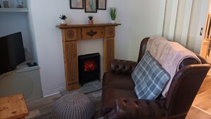 A living room with a fireplace, a leather sofa, a television, and a small wooden table. - Cosy Mews House Close to Harbour (Porthmadog)