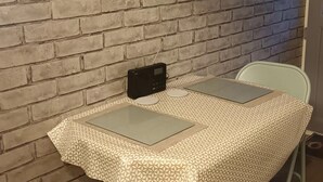 A small dining area with a brick wall, a table with a patterned tablecloth, two chairs, and a radio on the wall. - Cosy Mews House Close to Harbour (Porthmadog)