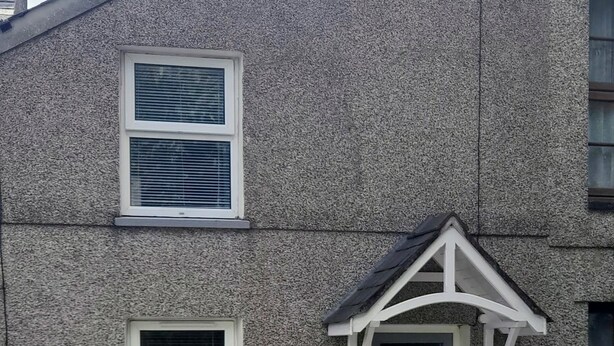 A stone building with a blue door, two windows with shutters, a small porch, and a white picket fence. - Cosy Mews House Close to Harbour (Porthmadog)