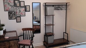 A bedroom with a wooden chair, a bedside table, a mirror, a wardrobe, and wall-mounted artwork. - Cosy Mews House Close to Harbour (Porthmadog)