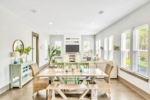 A spacious living area with a dining table, wicker chairs, a sofa, and large windows with blinds. - Private Pool - Golf Cart - Kid Friendly - Luxury (Miramar Beach)