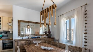 A modern kitchen with wooden cabinets, a dining table with chairs, and a hanging light fixture. - Villa Retreat (Milos)