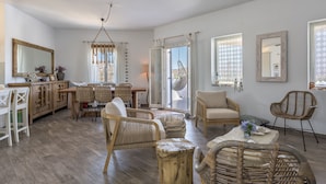 A spacious living room with a dining area, wicker furniture, and large windows with patterned curtains. - Villa Retreat (Milos)