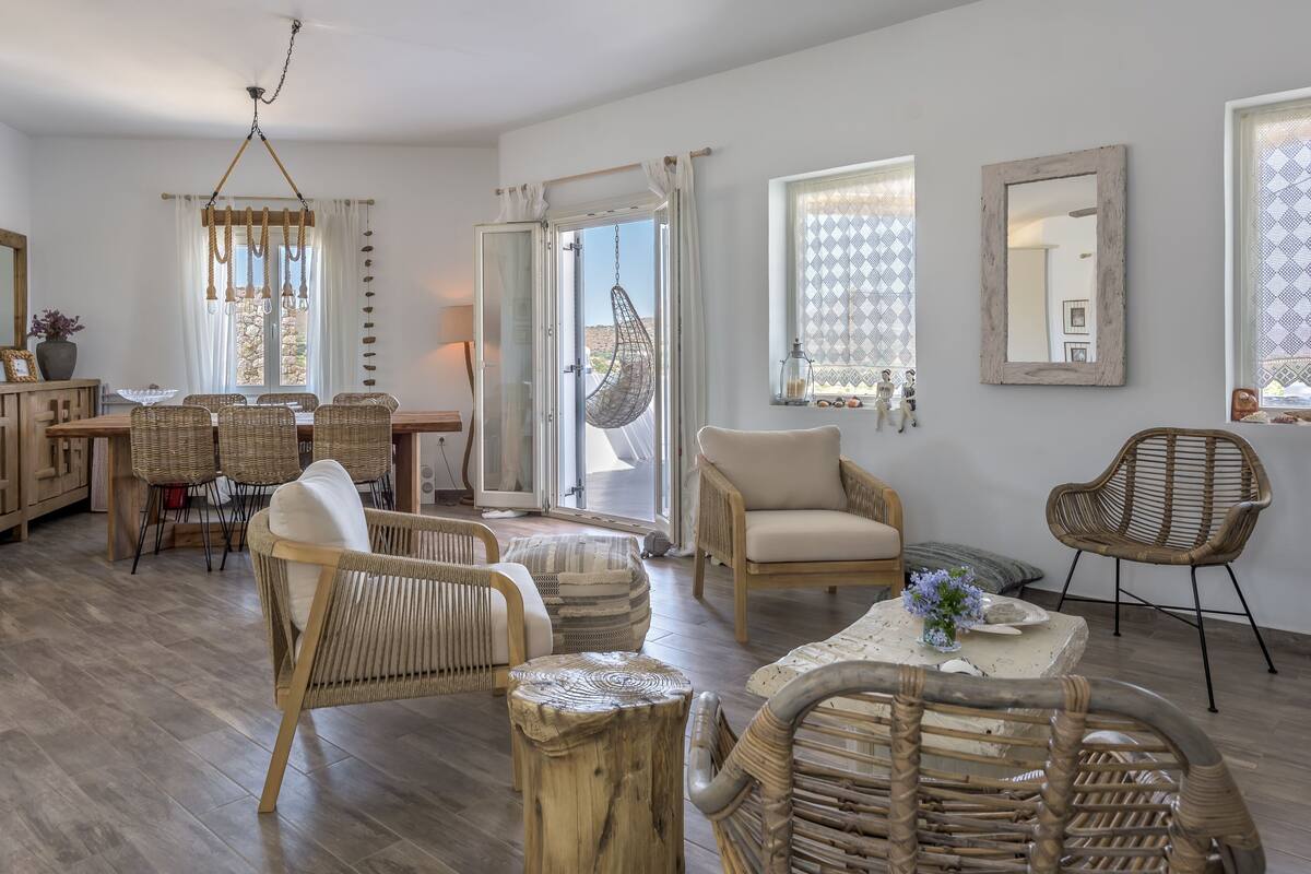 Tilava olohuone, jossa on ruokailutila, rottingista valmistetut huonekalut ja suuret ikkunat, joissa on kuvioidut verhot.