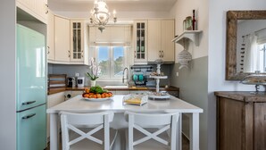 A kitchen with white cabinets, a teal refrigerator, a central island with chairs, and a chandelier. - Villa Retreat (Milos)