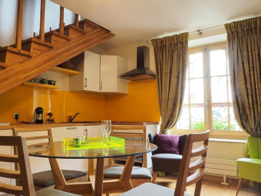 A kitchen with a wooden staircase, a dining table with chairs, and a window with curtains.