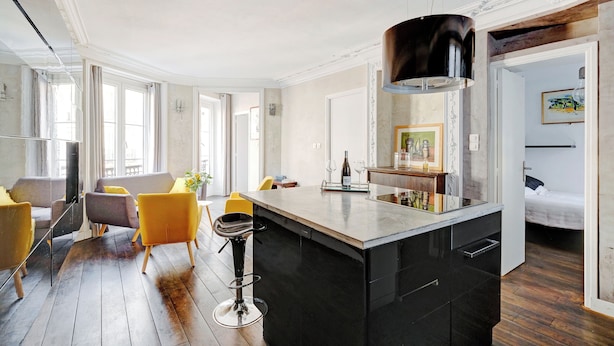 Een moderne keuken met een groot eiland, barstoelen en een eethoek met gele stoelen.