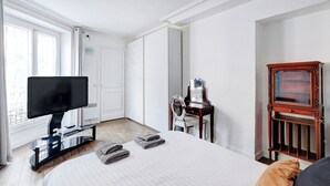 Hotelkamer met een bed, een televisie op een standaard, een spiegel, een houten kast en een raam met gordijnen.