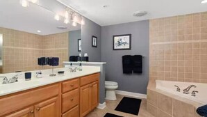 A modern bathroom with a large mirror, dual sinks, a toilet, and a bathtub.