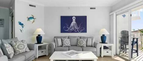 Un salon moderne avec un canapé gris, une table basse blanche et des œuvres d’art décoratives au mur.