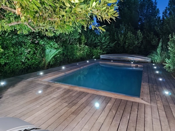 Une piscine rectangulaire dotée d’une terrasse en bois et entourée de verdure.