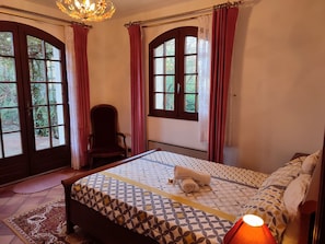 Une chambre à coucher avec un lit, une chaise et de grandes fenêtres avec des rideaux.