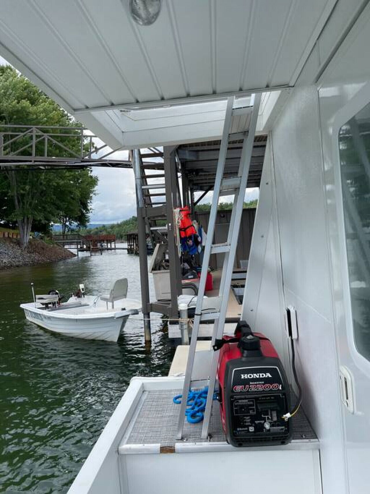 A boat with a ladder leading to a covered area, a Honda generator, and a small docked boat in the background.