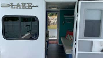 A camper with a window, a door leading to an outdoor area, and a bed with pillows.