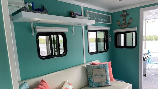 Una habitación color esmeralda con un banco blanco, dos ventanas con marcos negros y una puerta blanca que da al exterior.